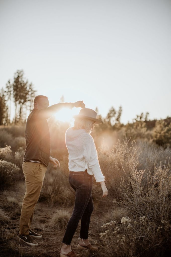 Guy spins girl as they stroll through the shrub lands during golden hour