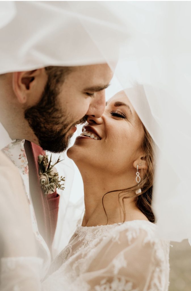 Choosing An Oregon Elopement Photographer: Everything You Need To Know. Bride and groom smile under the bride's veil during their elopement shoot captured by Morgan Wirth.