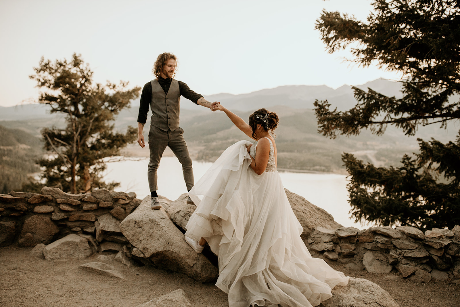 A groom reaches out to hold bride's hand as she steps up on a rock for their Adventurous Breckenridge Elopement photographed by Morgan Wirth Photography.
