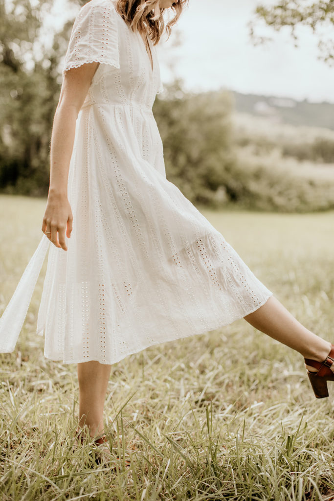 A girl in a white sundress walks through a field; image by Morgan Wirth Photography