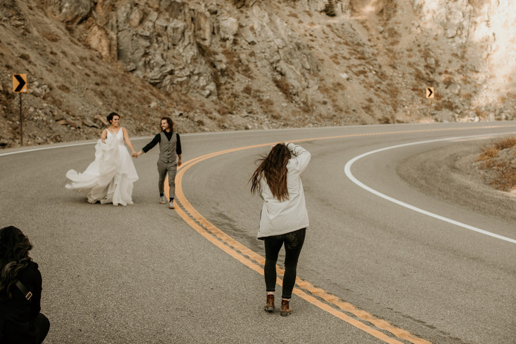 Oregon Wedding Photographer Morgan Wirth taking a photo of bride and groom as they stroll down an uphill highway