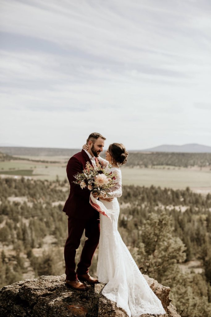 Couple hug and look at each other on top of a mountain during their elopement shoot in Oregon taken by Morgan Wirth