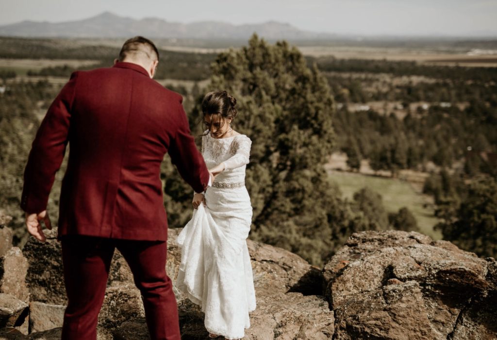 Choosing An Oregon Elopement Photographer: Everything You Need To Know. Groom helps bride climb up the mountain during their elopement shoot taken by Morgan Wirth Photography.