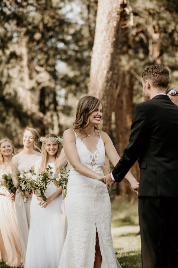Bride laughs along with the three bridesmaids behind her as she holds the groom's hand during their wedding ceremony at Aspen Lake Golf Course