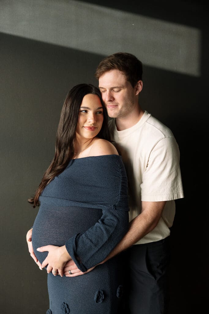Expecting couple embracing during a maternity shoot in a Dallas natural light studio.