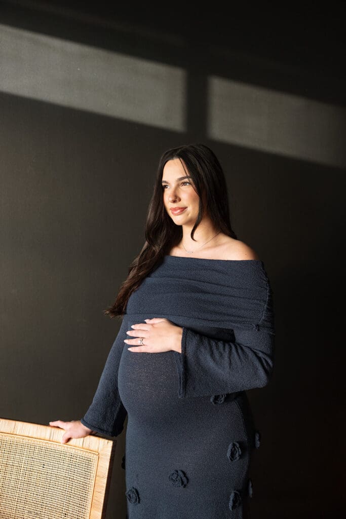 Mother-to-be looking out the window, sunlight streaming in, Dallas maternity studio session.