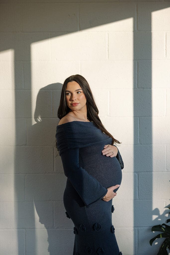 Close-up maternity detail of baby bump with natural sunlight in a Dallas studio.