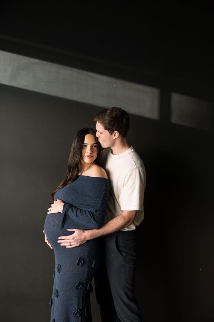 Couple standing together, hands on baby bump, during a Dallas maternity studio session.