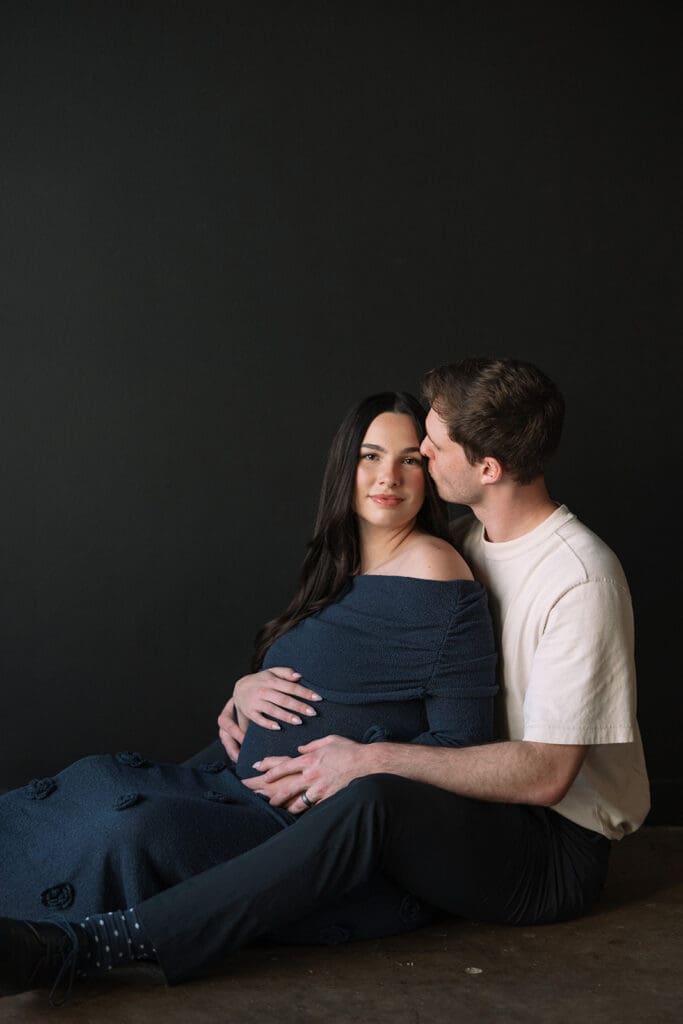 Couple sitting together on the floor, embracing in a cozy documentary-style maternity session in Dallas.