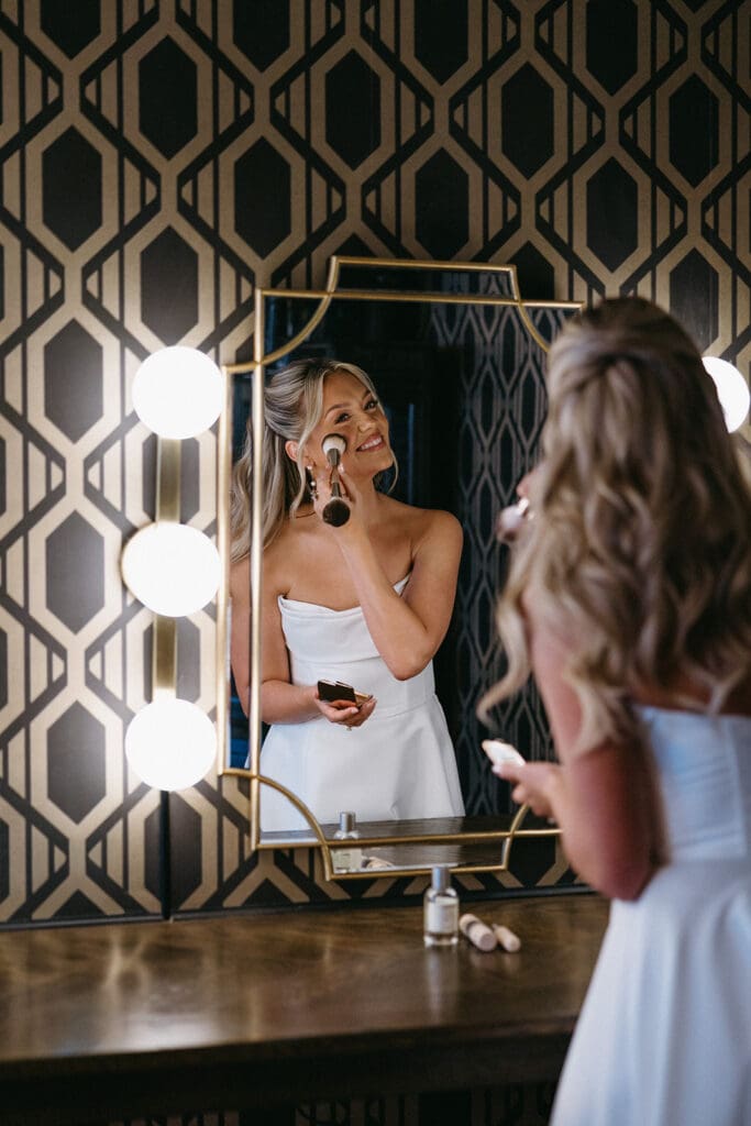 Bride touching up makeup in the mirror at The Mason wedding venue in Dallas